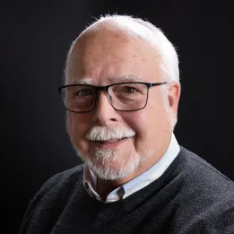 A male with white hair, beard and glasses